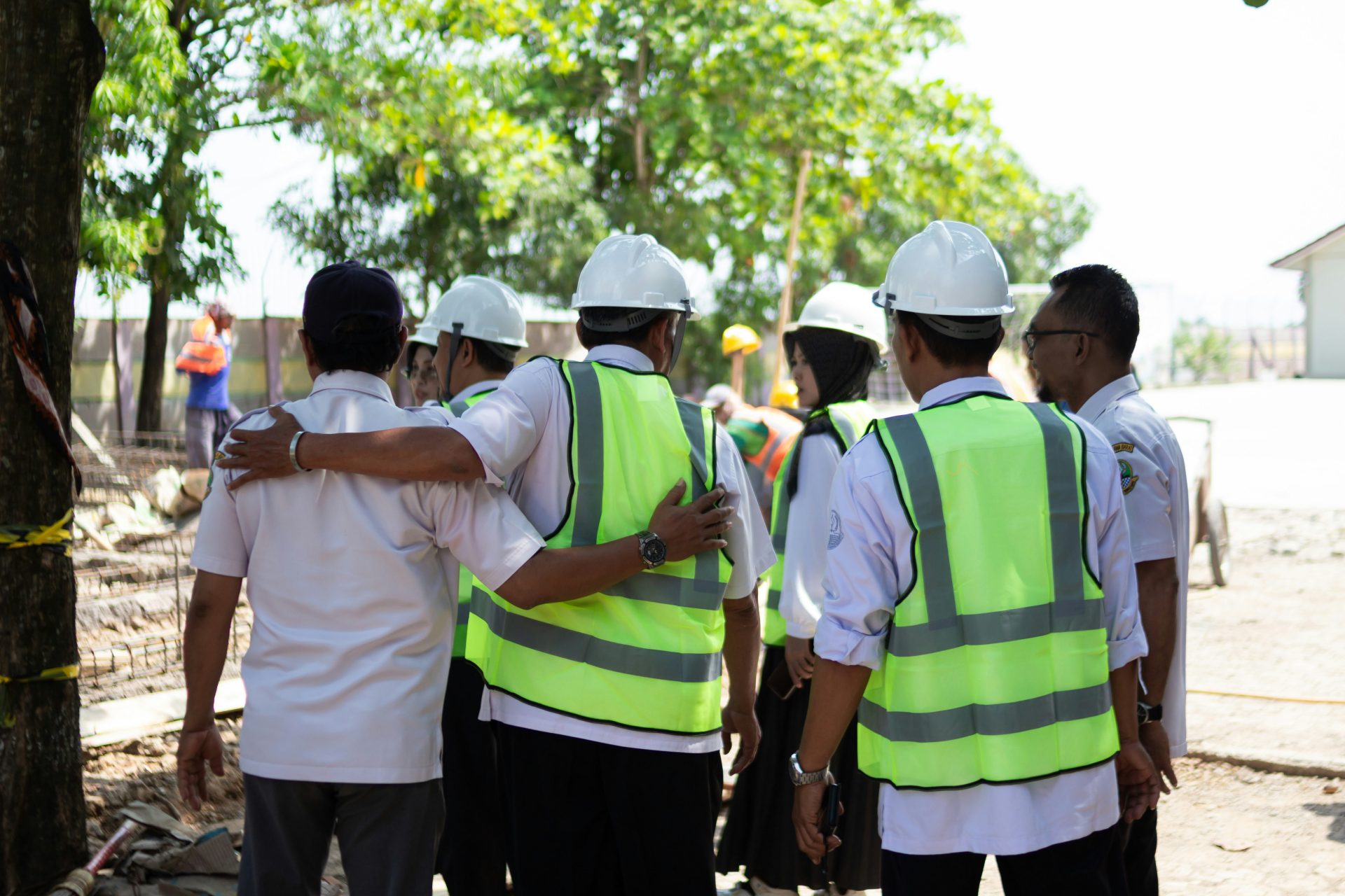 Construction workers in hard hats and vests huddle together.